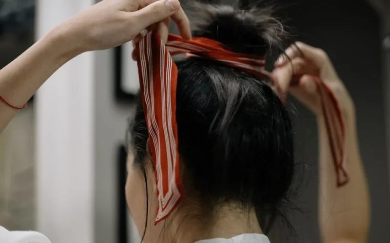 Close-up of a woman styling her hair with a red scarf indoors, showcasing hairstyling technique.