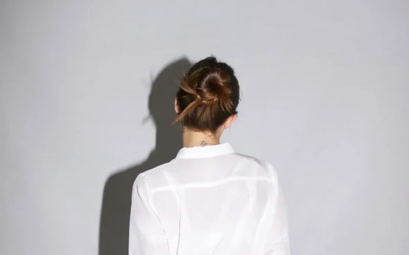 Studio shot of a woman in a white shirt with a hair bun casting a shadow.