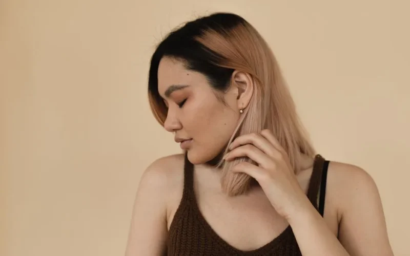 Portrait of an Asian woman with colored hair, eyes closed, posing against a beige background in a studio.