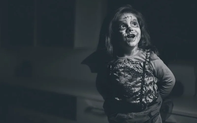 A happy child dressed in a spider web costume with face paint, smiling during Halloween.