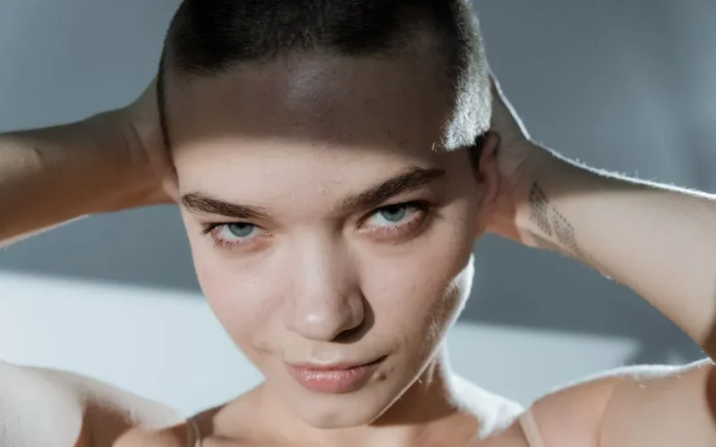 Close-up of a confident woman with a buzz cut, posing in studio light.