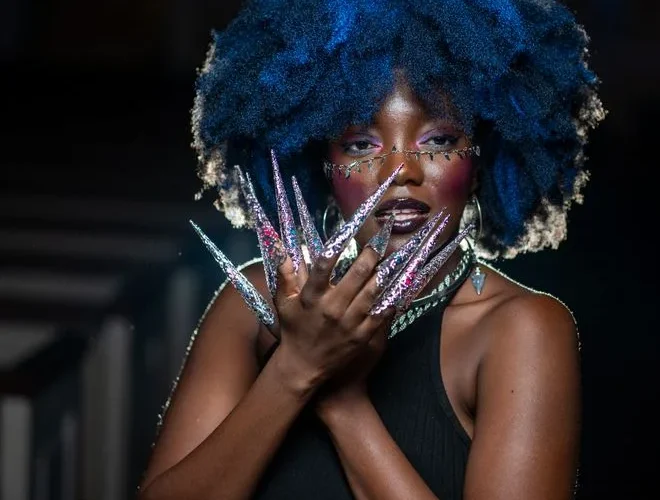 Striking portrait of a woman showcasing vibrant blue hair and elaborate artistic nail art.