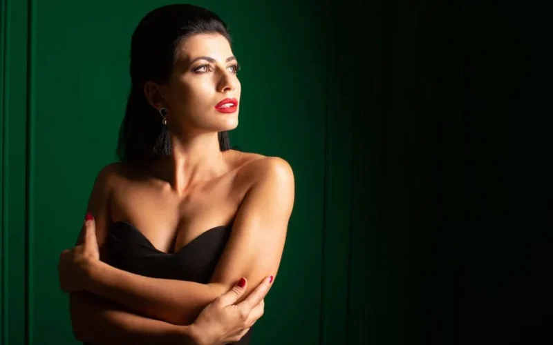 Portrait of an elegant woman with red lips, wearing a black dress and looking away, in dramatic lighting.