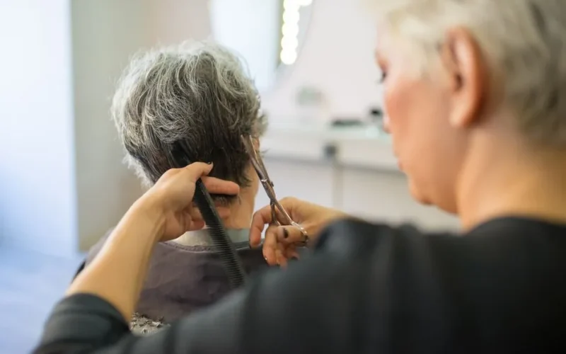 A hairstylist giving a senior woman a haircut in a modern salon setting.
