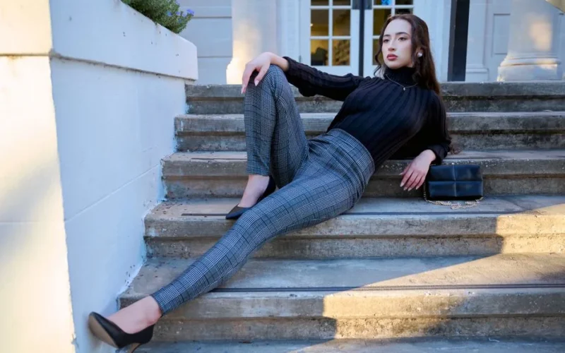 Fashionable woman in a black sweater and plaid pants posing on stone steps outdoors.