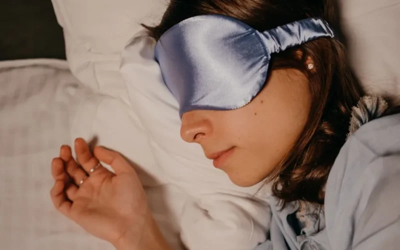 A woman wearing a silk eye mask sleeping peacefully on a pillow.
