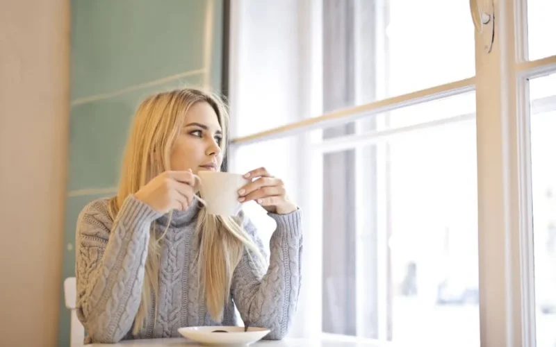 A woman with blonde hair enjoys a warm coffee in a cozy indoor cafe setting.