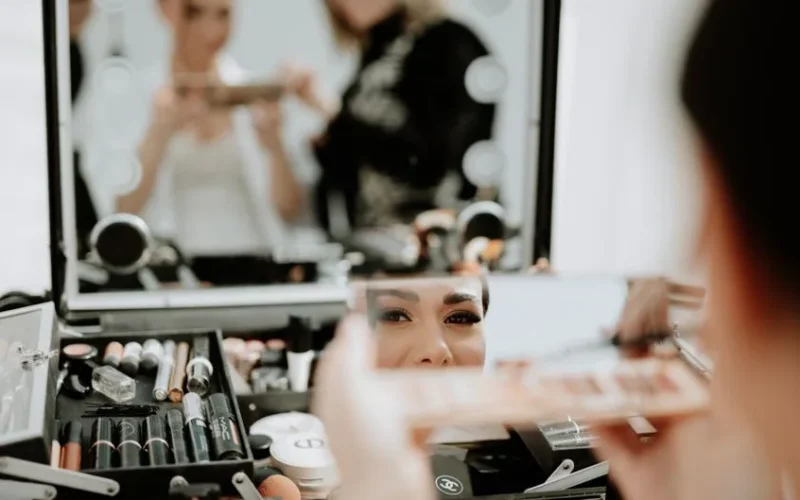 Bride getting her makeup done with a beautician in front of a mirror. Focus on reflection.