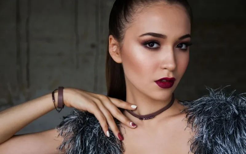 Close-up portrait of an elegant woman with bold makeup and fashionable attire, exuding confidence.