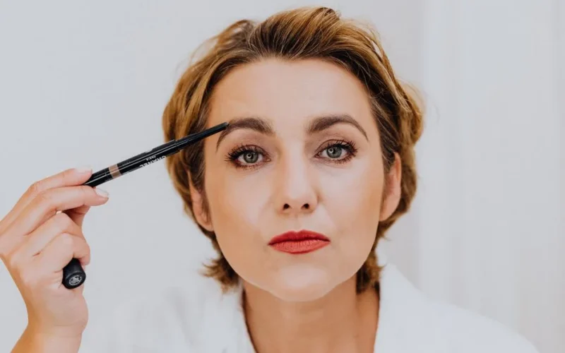 A close-up portrait of a woman applying eyebrow pencil, showcasing beauty and elegance.