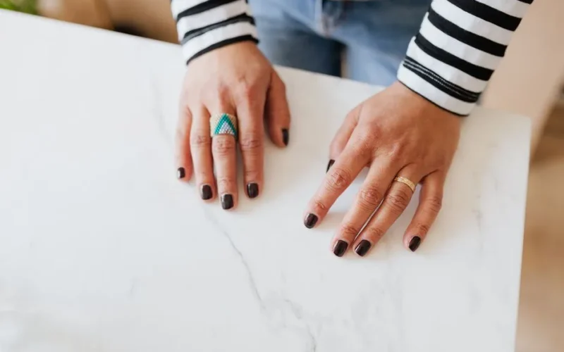 From above unrecognizable woman demonstrating hands with manicured nails on white table in apartment during weekend