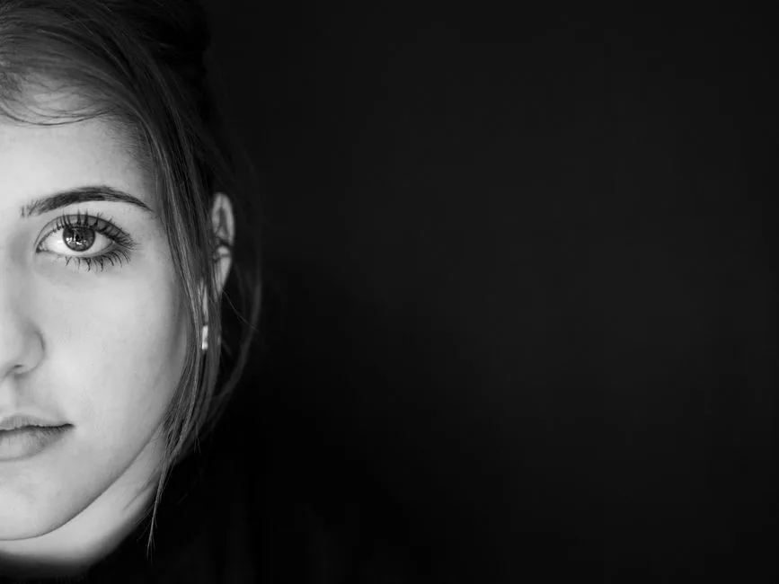 Half-face black and white portrait of a woman against a dark background.