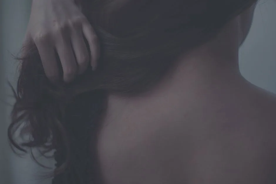 Artistic close-up of a woman gently touching her hair, capturing soft textures and intimate mood.