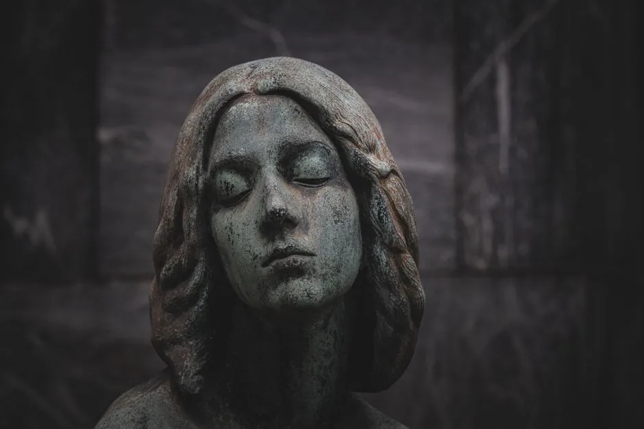 Close-up of a serene stone statue with a green patina finish, set against a dark background.