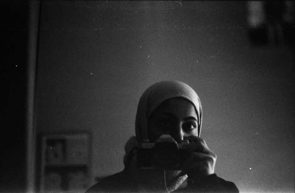 Artistic black and white self-portrait of person holding a camera.