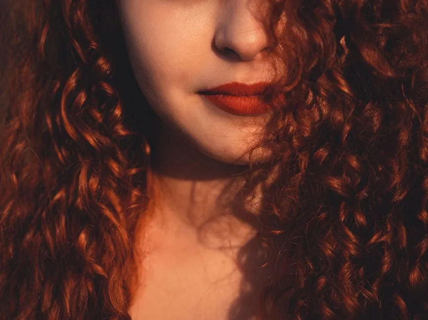 Unrecognizable beautiful female with dark reddish fluffy hair and vivid red lips in daylight