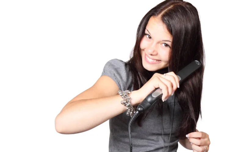 young woman using her hair straightener isolated on white background
