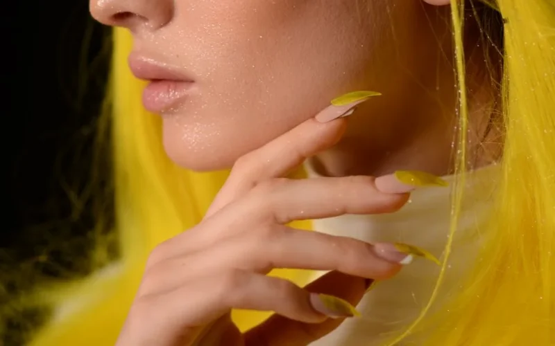 Artistic close-up of a woman with glitter, yellow hair, and nails, highlighting fashion and style.