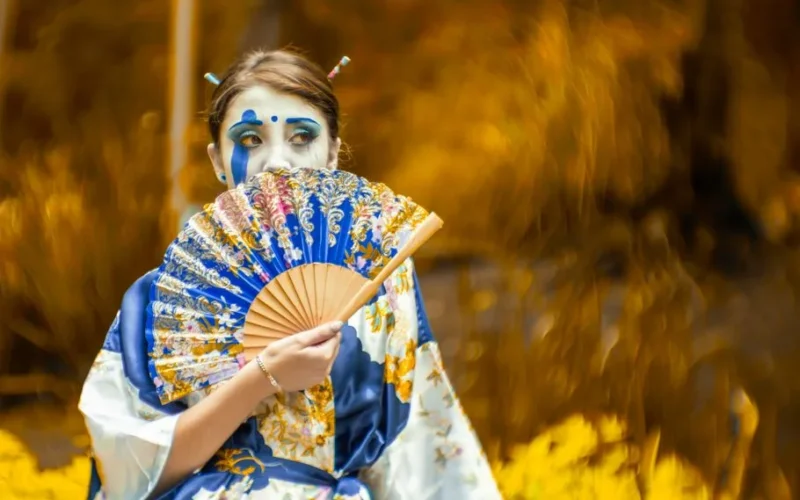 A stunning portrait showcasing a woman in traditional Japanese attire with striking makeup, outdoors.