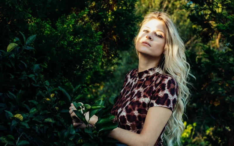 Blonde woman in animal print shirt posing amidst greenery, Curitiba, Brazil.