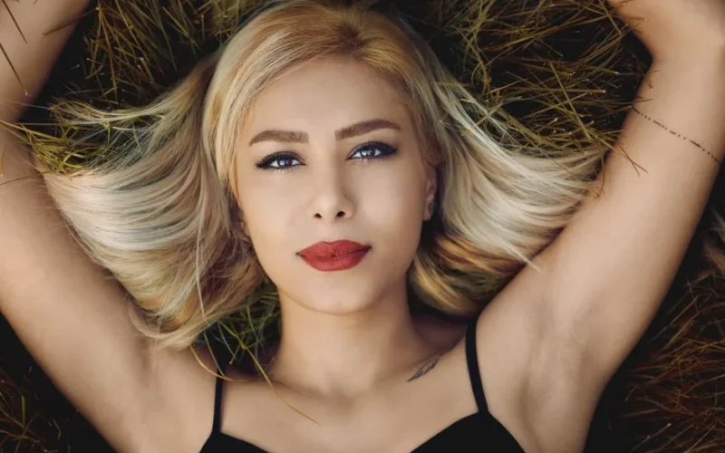 Beautiful blonde woman with red lips lying on grass in a relaxed pose.