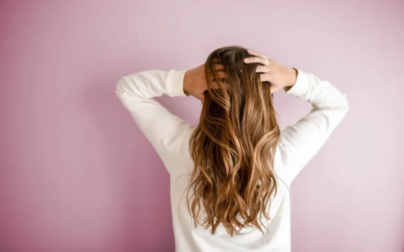 Back view of a woman with elegant long brown hair against a pink wall, showcasing stylish hair design.