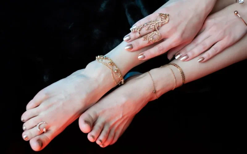 Crop anonymous female legs and hands with stylish manicure and pedicure wearing oriental golden bracelets anklets and rings