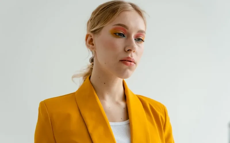 Portrait of a woman in a yellow blazer with vibrant eyeshadow.