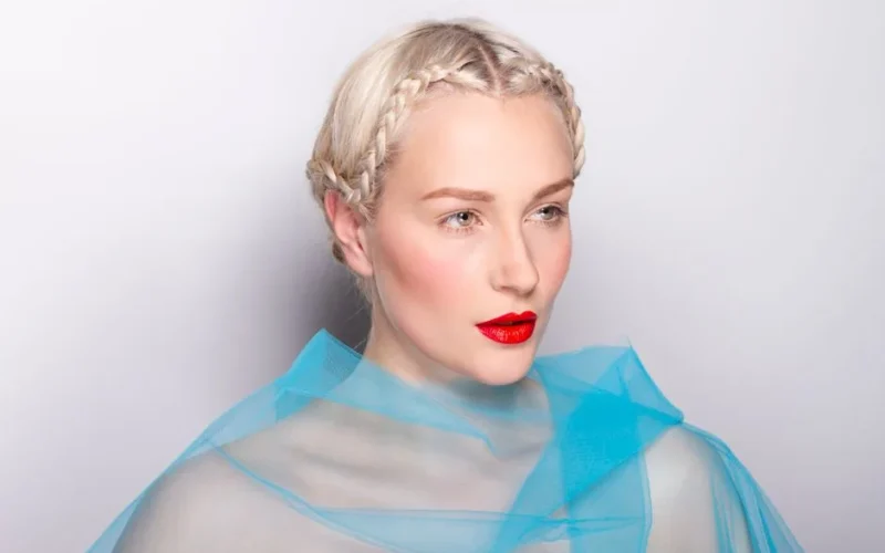 Portrait of a woman with braided hair and red lips against a white background.