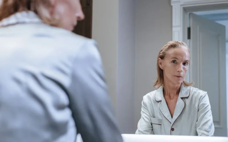 Elderly woman with blond hair looking at her mirror reflection in bathroom.