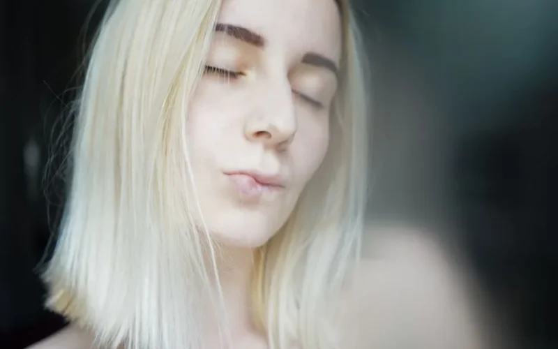 Crop pretty young woman with blond hair and dark eyebrows delicately pursing lips