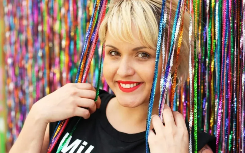 Vibrant portrait of a smiling blonde woman with red lipstick surrounded by colorful sequins.