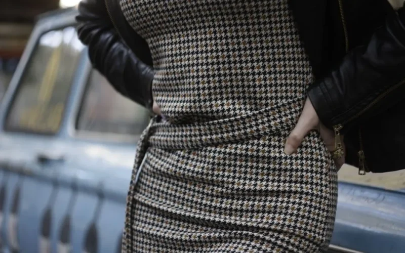 Close-up of a woman in a houndstooth dress and leather jacket outdoors.