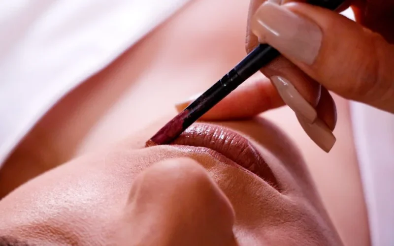 Crop female with makeup and manicure putting lip liner on lips in daylight