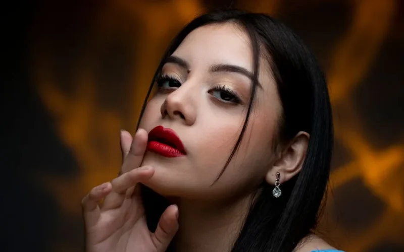 Close-up portrait of a woman with bold red lipstick and elegant earrings.