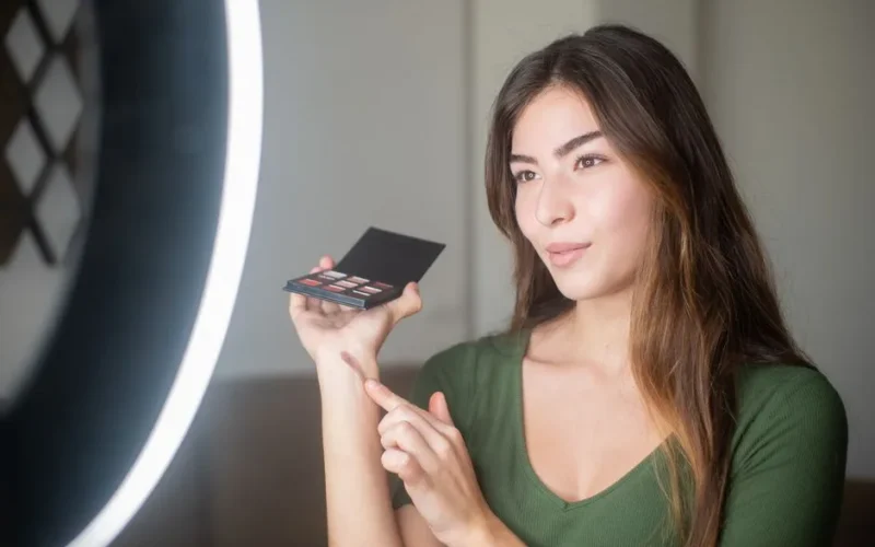 Young woman influencer applying makeup in well-lit indoor setting, showcasing beauty products.