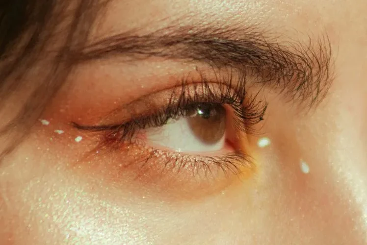 Detailed close-up of a woman's eye with shimmering makeup and artistic accents.