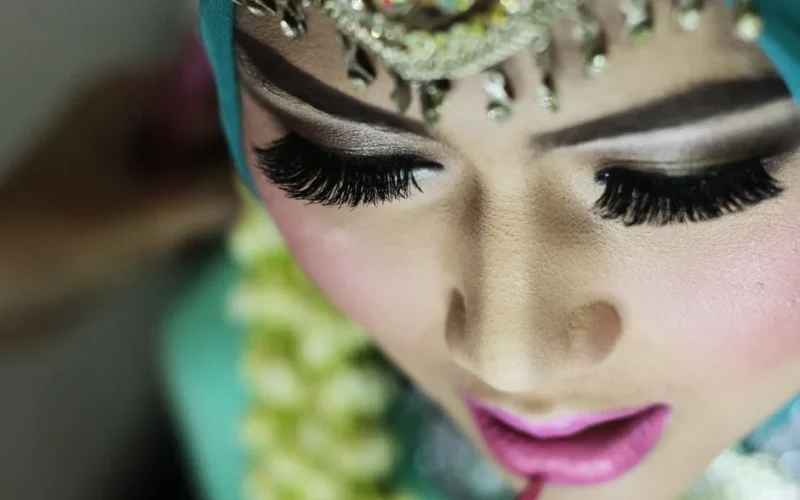 Detailed close-up of a woman applying makeup, focusing on her eye makeup and lips.