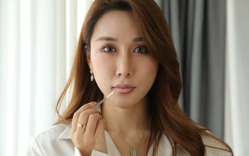 Elegant woman applying lip gloss, highlighting beauty and cosmetic products.