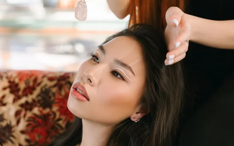 Asian woman with elegant makeup and crystal pendant, indoors setting.
