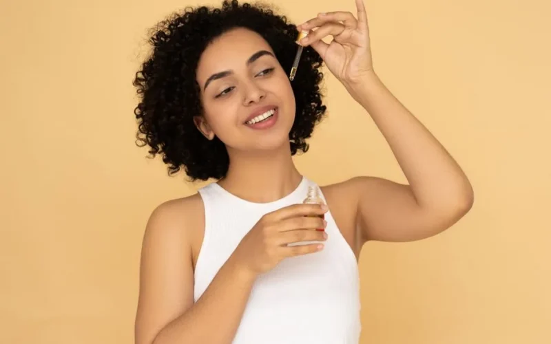 A woman with curly hair applies essential oil on her skin, promoting wellness and skincare.