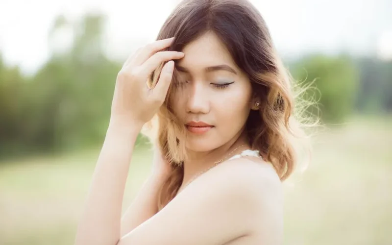 Elegant woman with closed eyes posing gracefully in a natural setting.