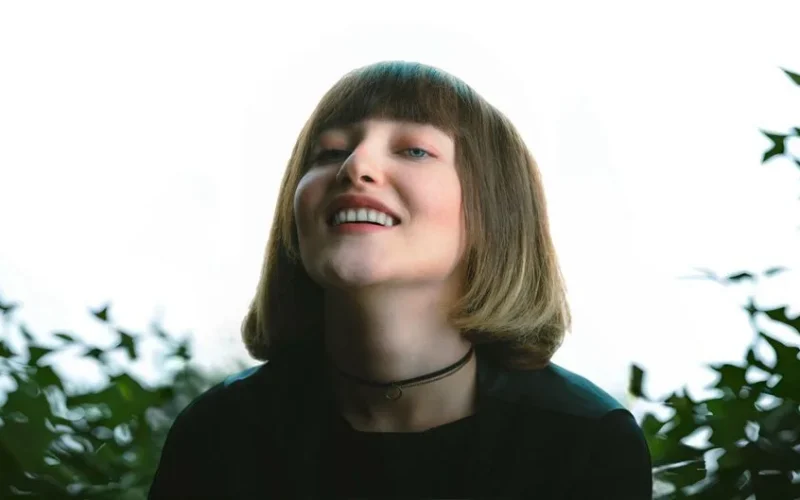 Close-up of a smiling woman with a bob haircut against a bright outdoor background.