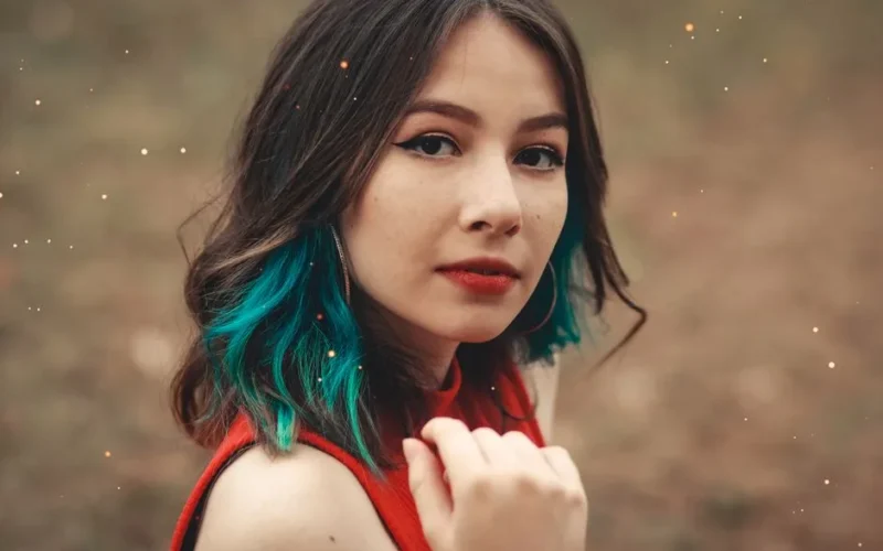 Close-up of a fashionable young woman with blue highlights posing outdoors.