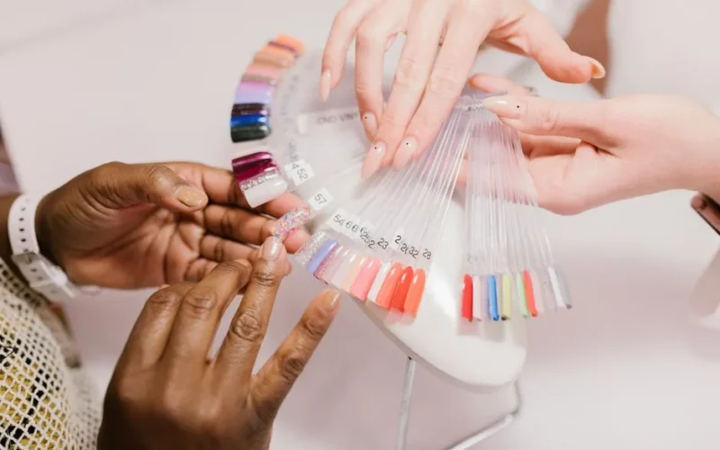 Close-up of hands choosing from a vibrant nail polish sample palette in a salon setting.