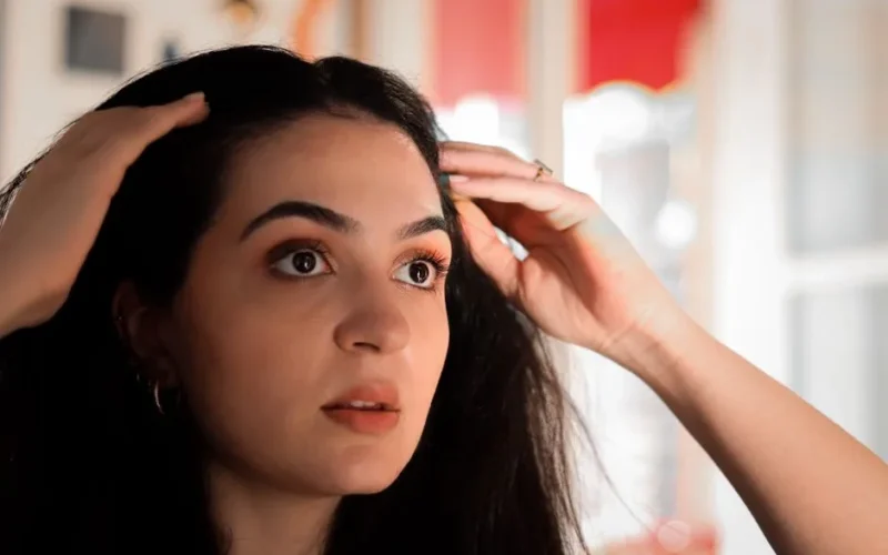A young woman indoors touching her hair, captured in a warm, intimate setting.