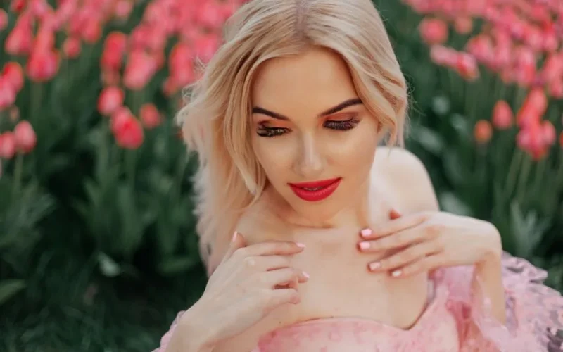 Portrait of a woman with blonde hair and vibrant lipstick surrounded by blooming tulips.