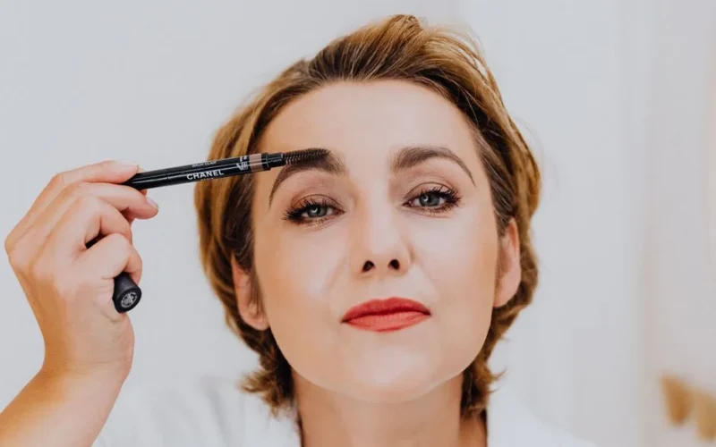 Portrait of a woman applying makeup with an eyebrow pencil, showcasing elegance.