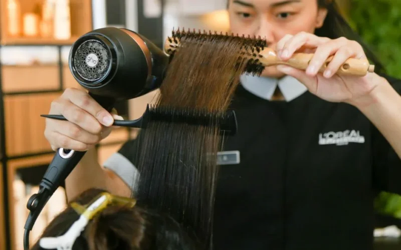 Hairdresser expertly styles hair using a brush and dryer in a salon setting.
