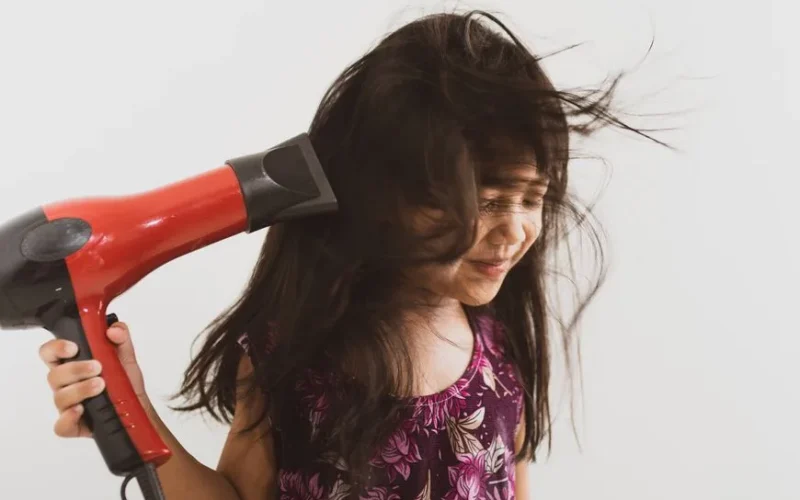 A happy girl using a hairdryer with her long hair blowing, indoors.